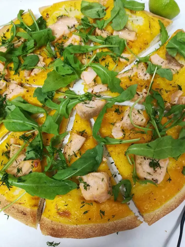 Pizza z kawałkami łososia, rukolą i koperkiem na żółtym sosie