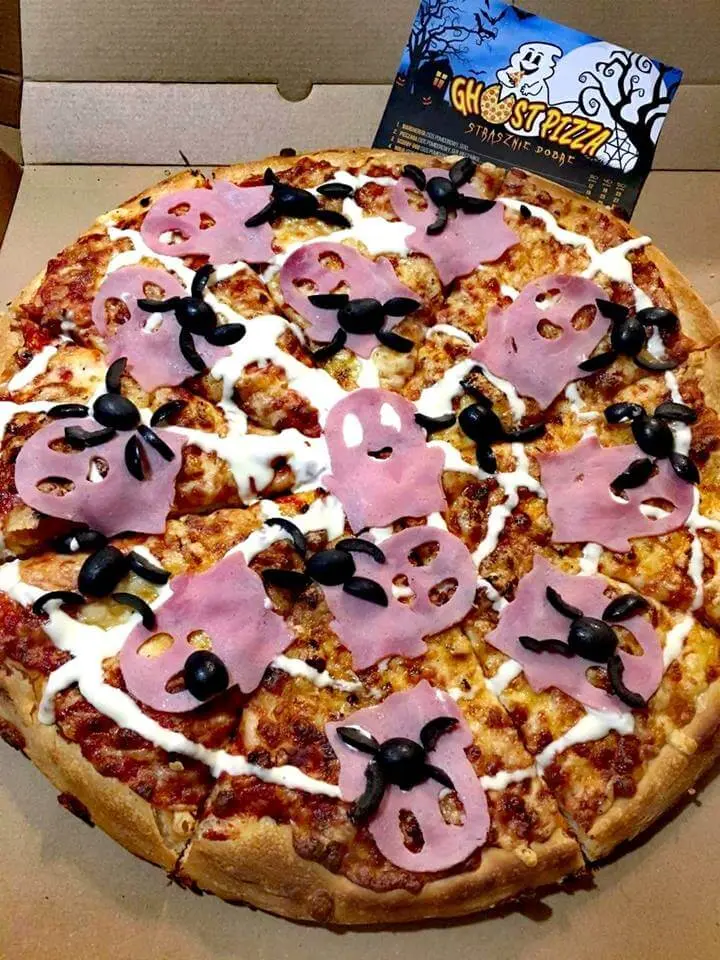 Pizza z szynką wyciętą w kształt duszków i pająkami z oliwek, obok ulotka Ghost Pizza