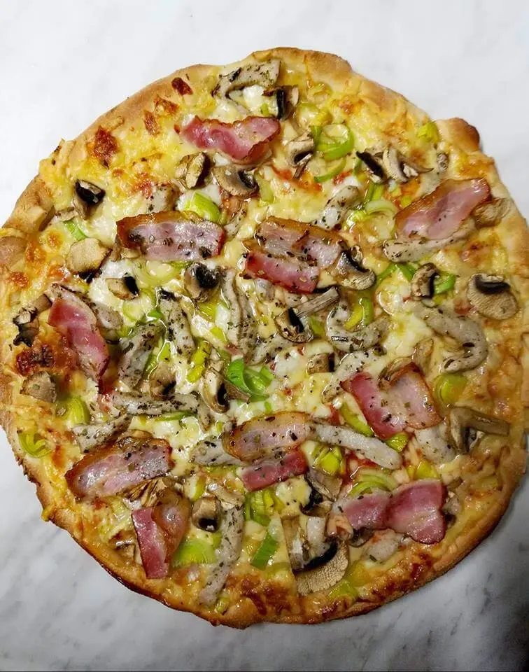 Pizza z boczkiem, kurczakiem, pieczarkami i porem na marmurowym blacie