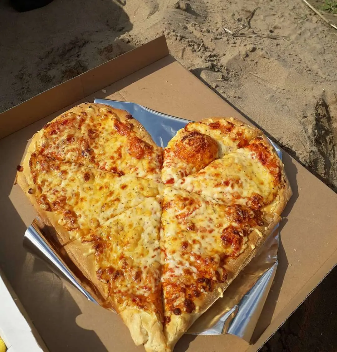 Pizza z serem w kształcie serca w kartonowym pudełku na piasku
